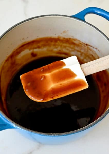 A spatula coated in easy homemade teriyaki sauce above a saucepan with sauce.