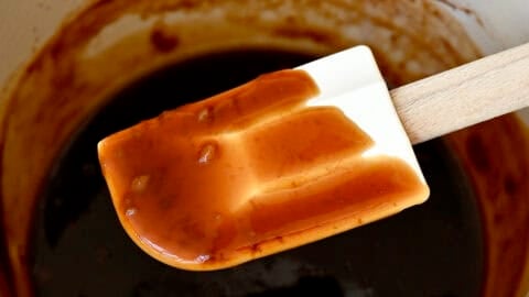 A spatula coated in easy homemade teriyaki sauce above a saucepan with sauce.