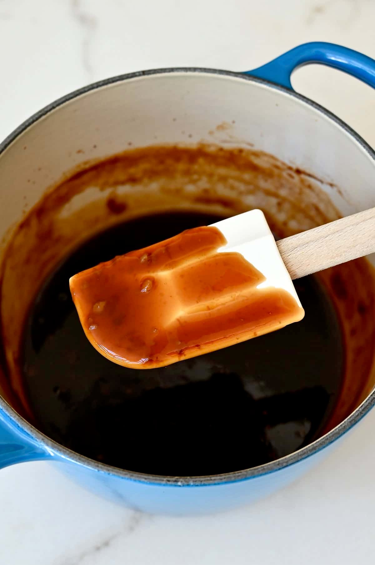 A spatula coated in easy homemade teriyaki sauce above a saucepan with sauce.