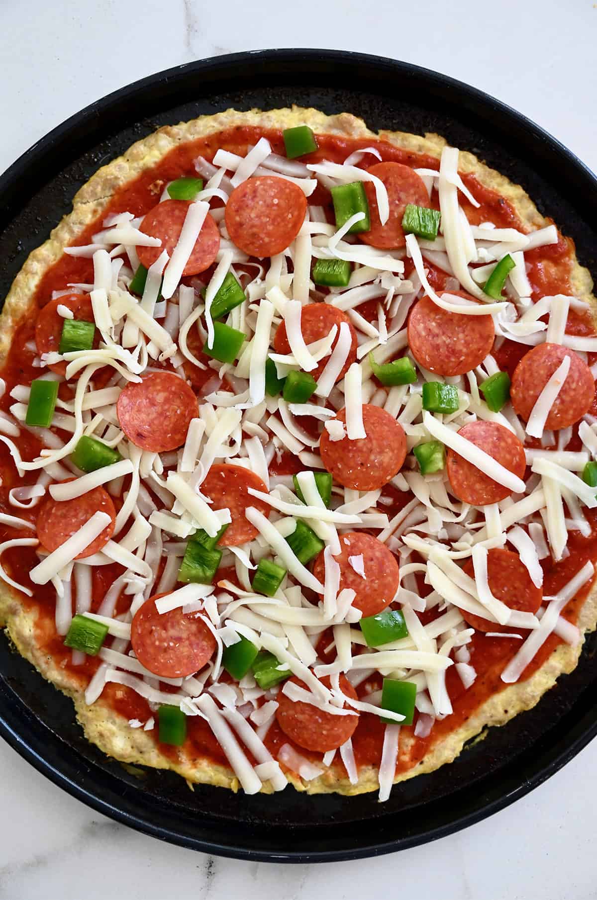 Sauce and toppings added to a chicken crust pizza before going back into the oven for its final bake.