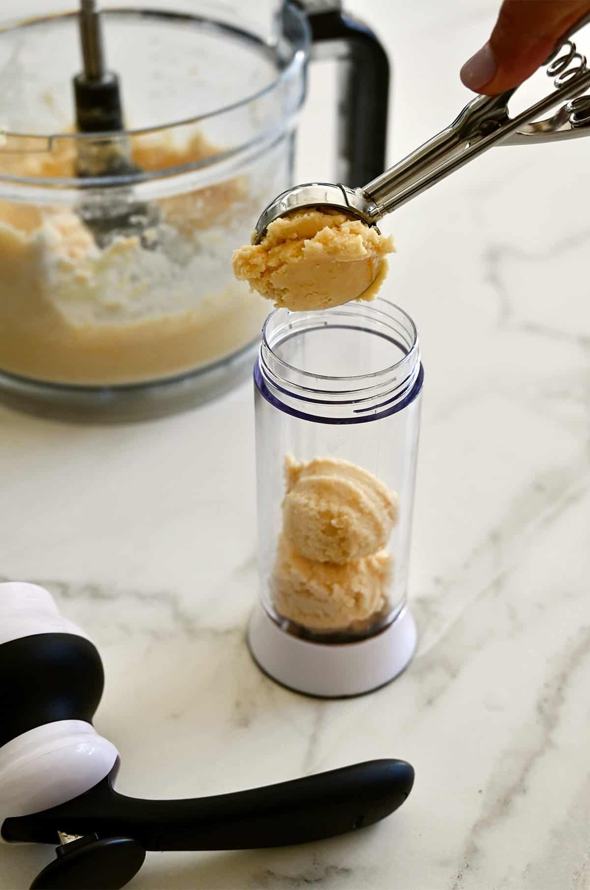Adding cheddar cracker dough to a cookie press with a small ice cream scoop.