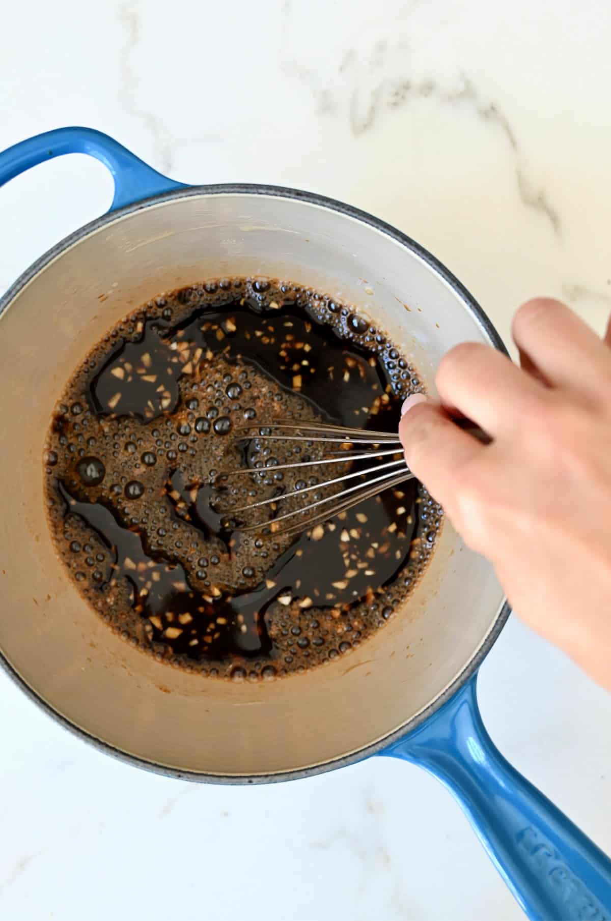 Whisking teriyaki ingredients together in a saucepan.