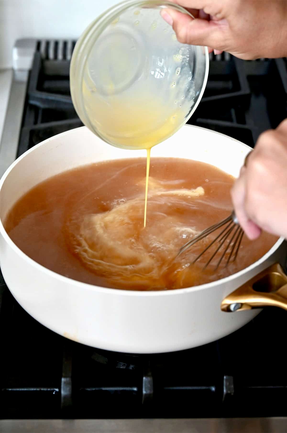 Whisking raw eggs into a stock pot containing hot broth.