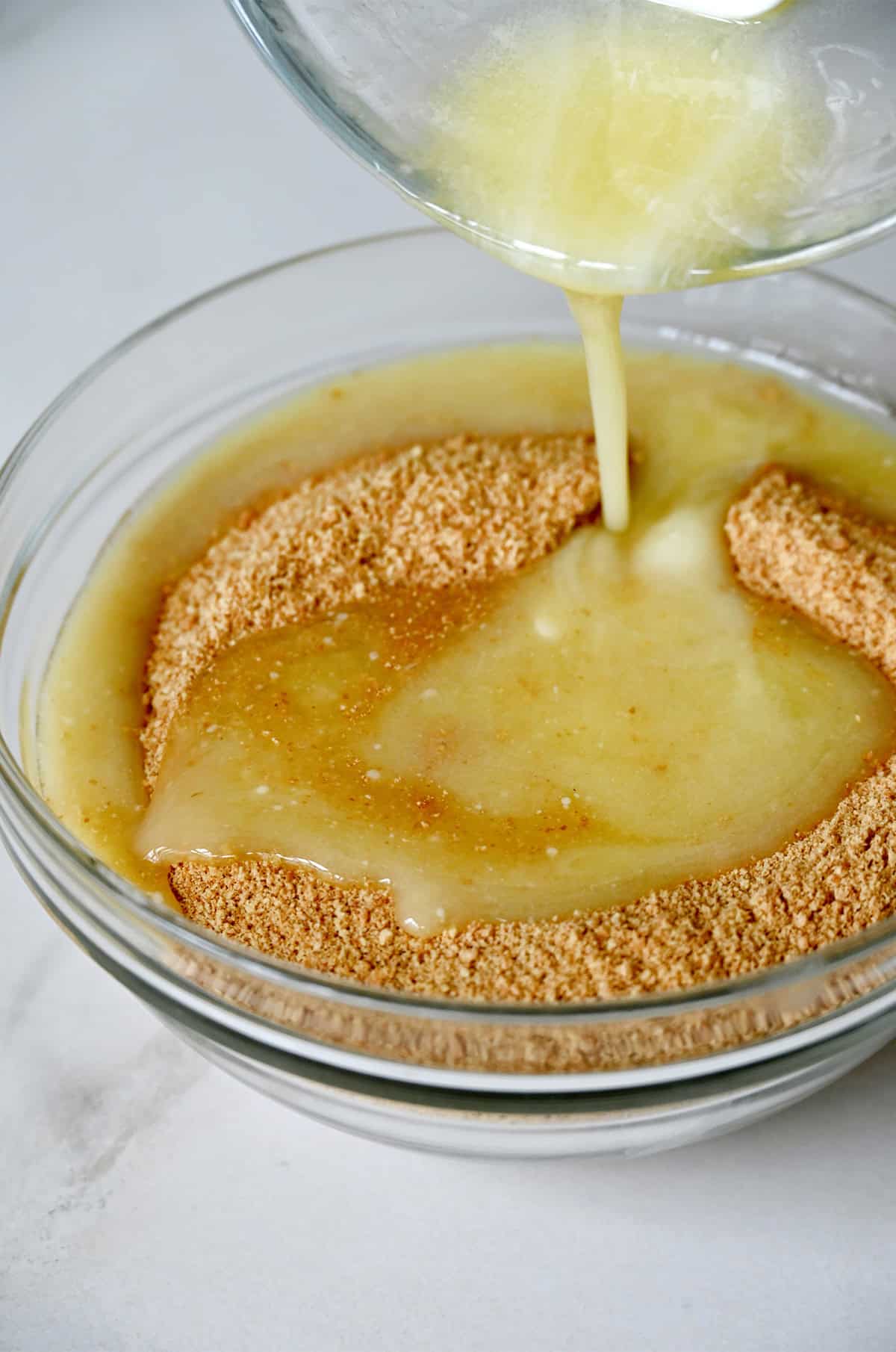 Melted butter being poured into a bowl with crushed graham crackers.