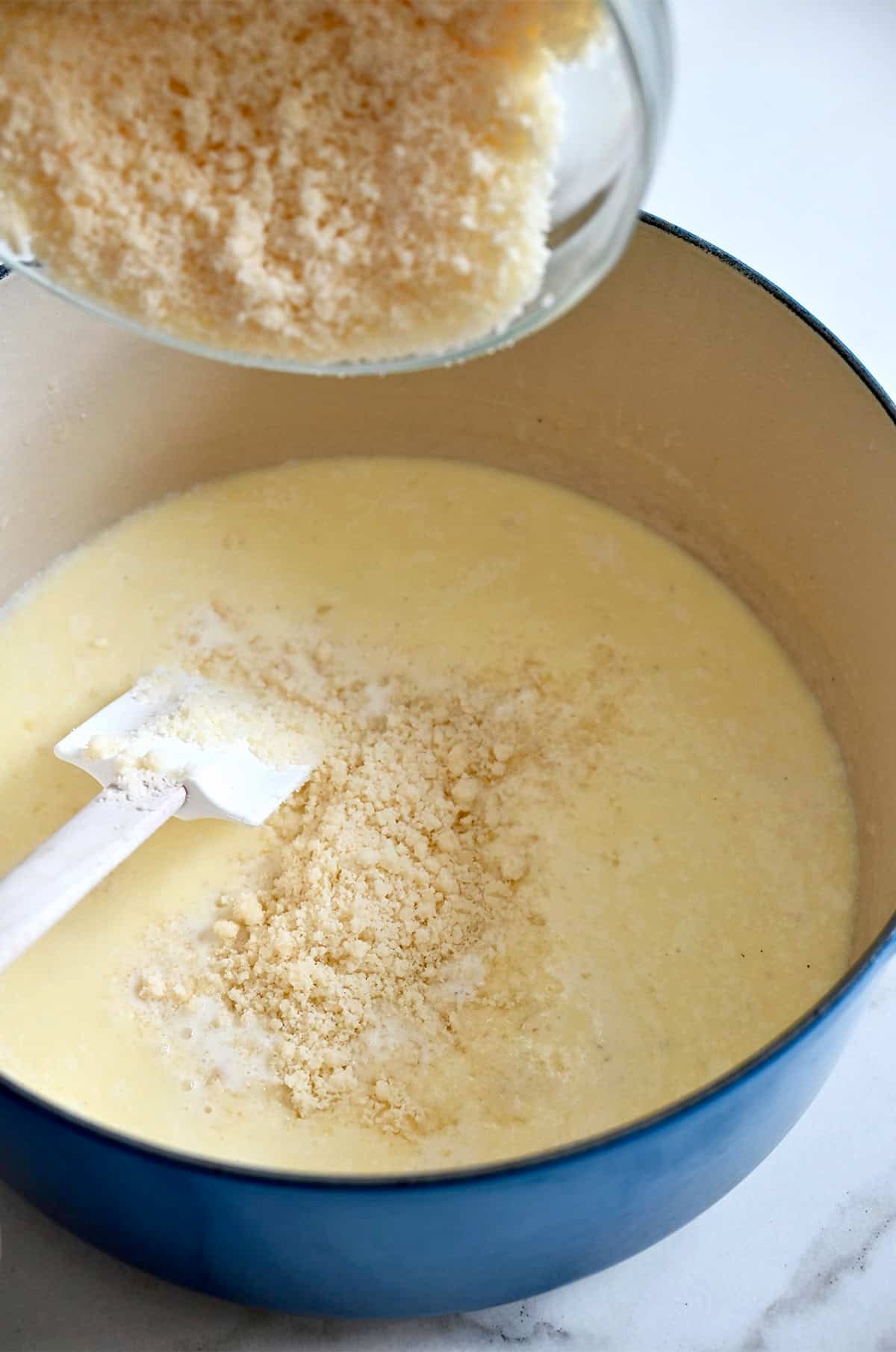 Adding grated Parmesan cheese to a large pot with heavy cream, melted butter and minced garlic to make an authentic Alfredo sauce.