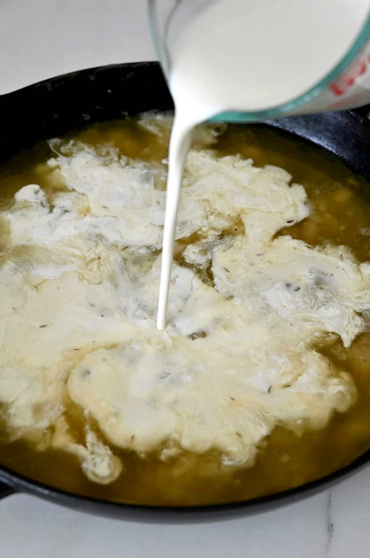 Adding heavy cream to a large skillet contianing a roux and chicken stock.