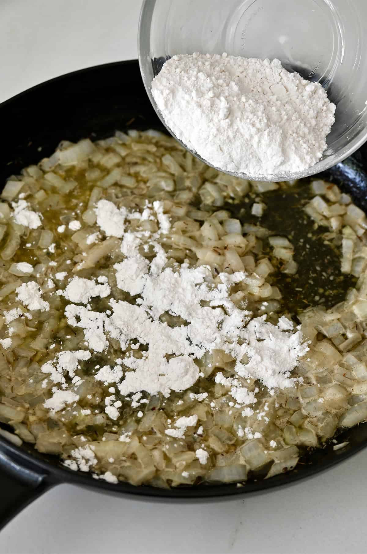 Flour being stirred into butter and onions to form a roux for chicken pot pie filling.