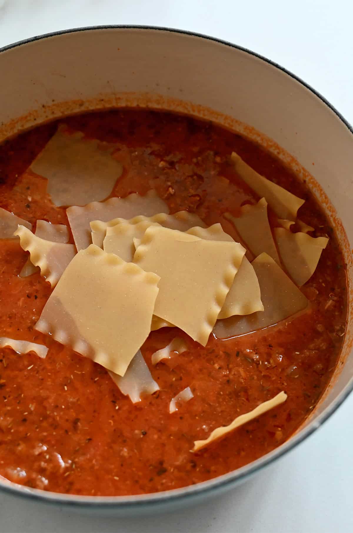 Broken lasagna noodles cooking in a marinara and chicken stock broth in a Dutch oven.