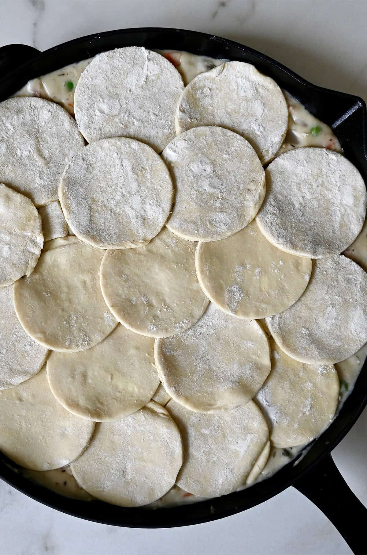 Adding puff pastry atop a skillet pot pie before baking.