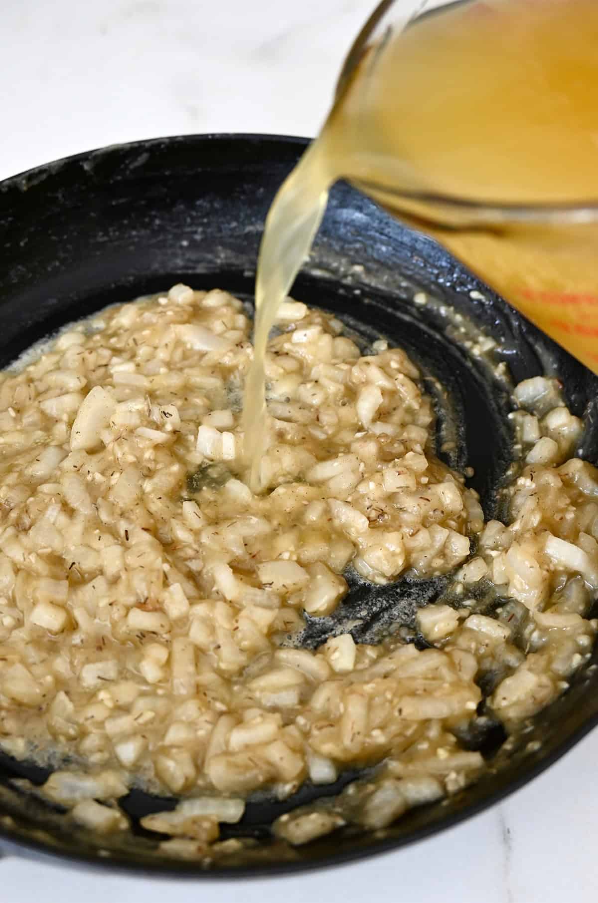 Adding chicken stock to a skillet with a roux.