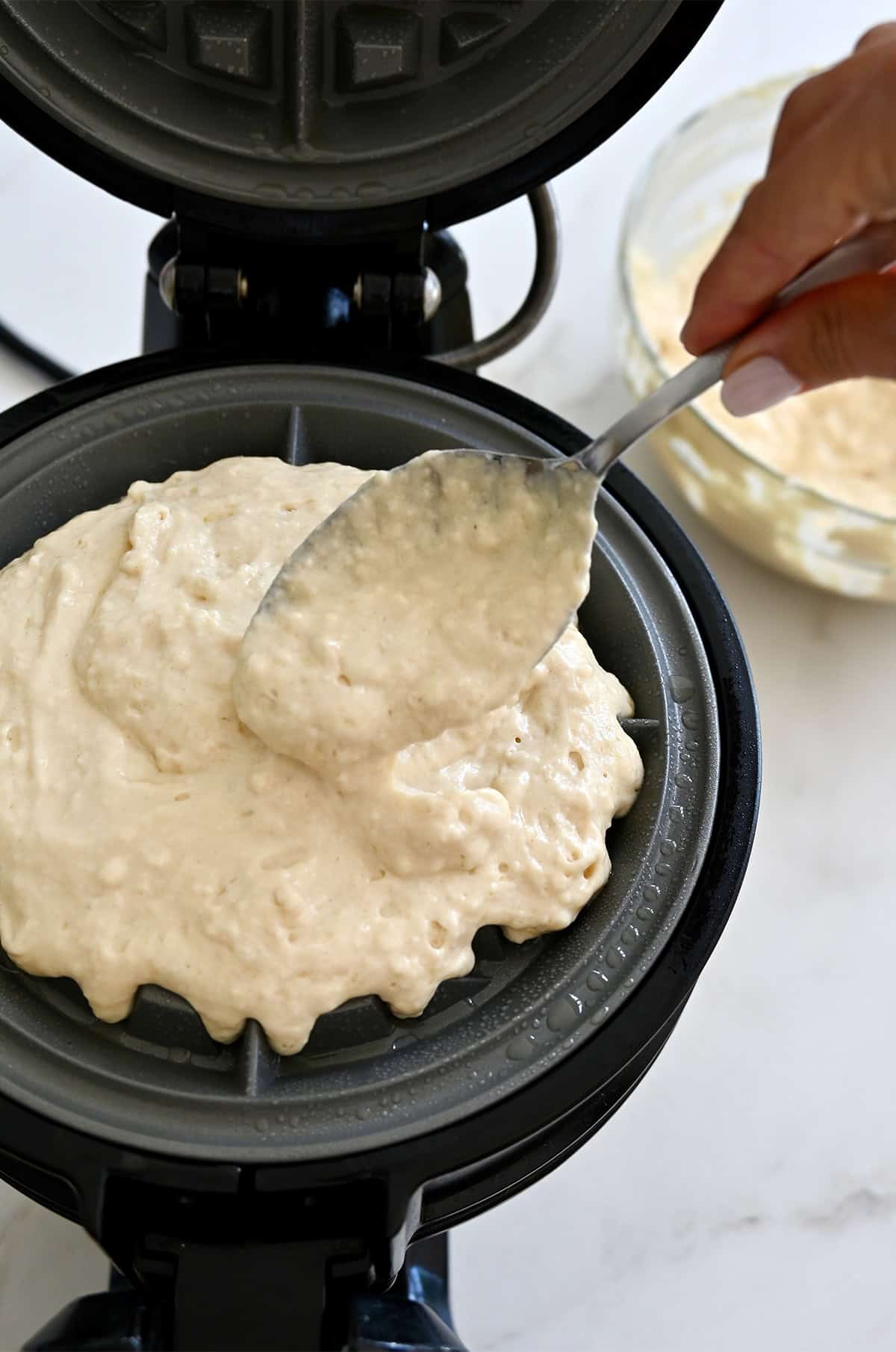 Spooning cottage cheese waffle batter into a preheated Belgian waffle maker. 