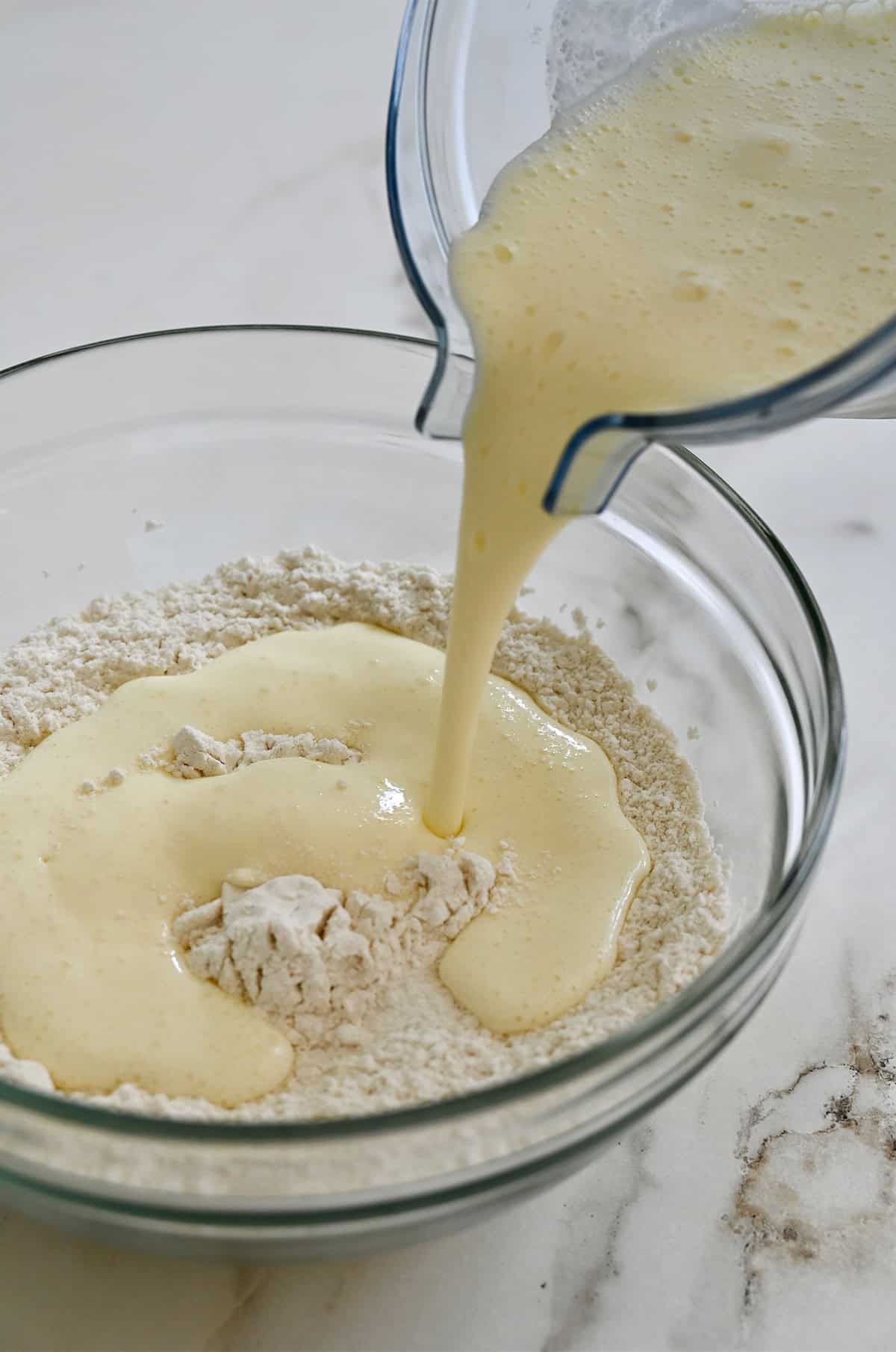 Adding wet ingredients from a blender to a bowl of dry ingredients.
