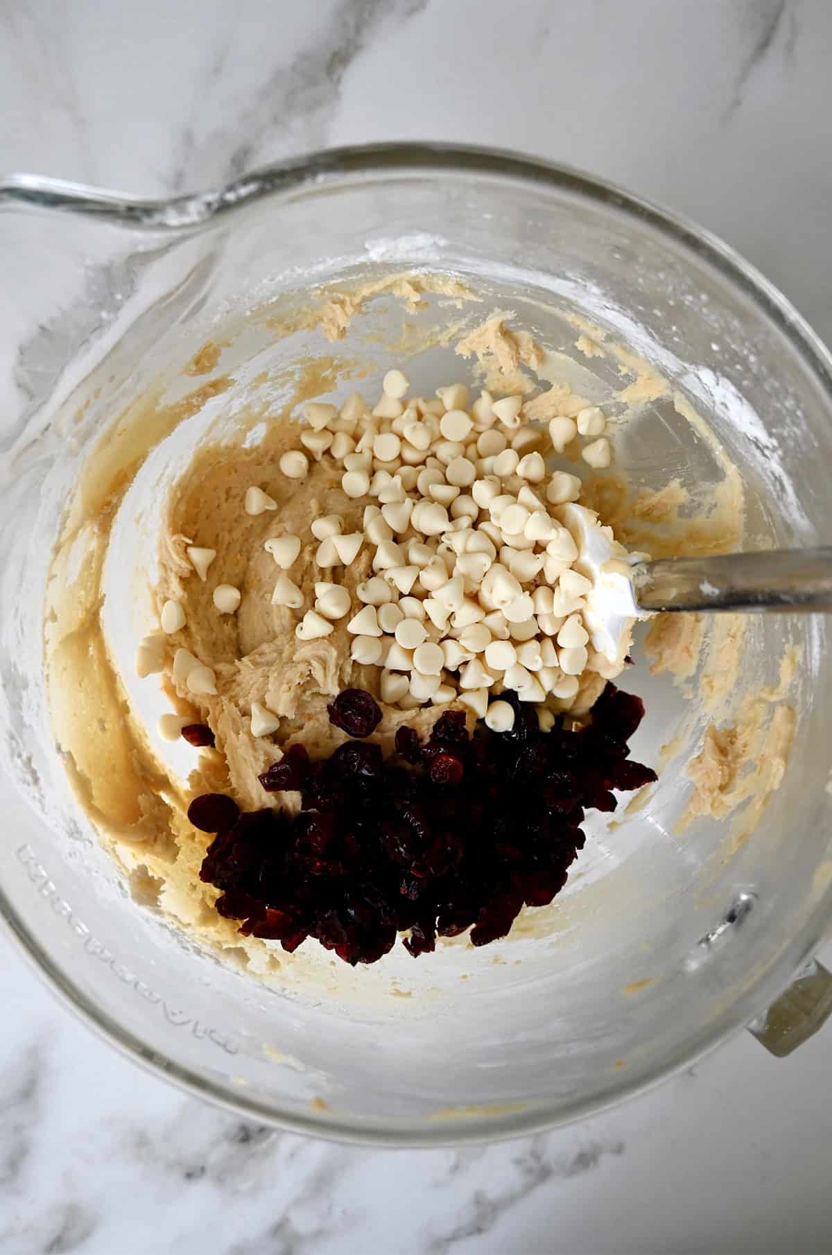 Blondie batter in a large glass bowl with white chocolate chips and dried cranberries.