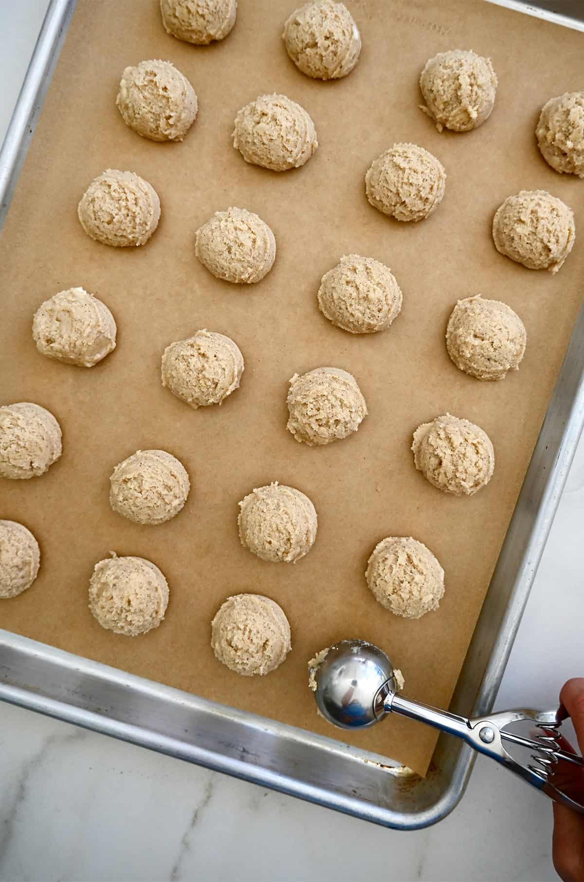 Perfect scoops of spiced sugar cookie dough on a parchment paper-lined baking sheet.