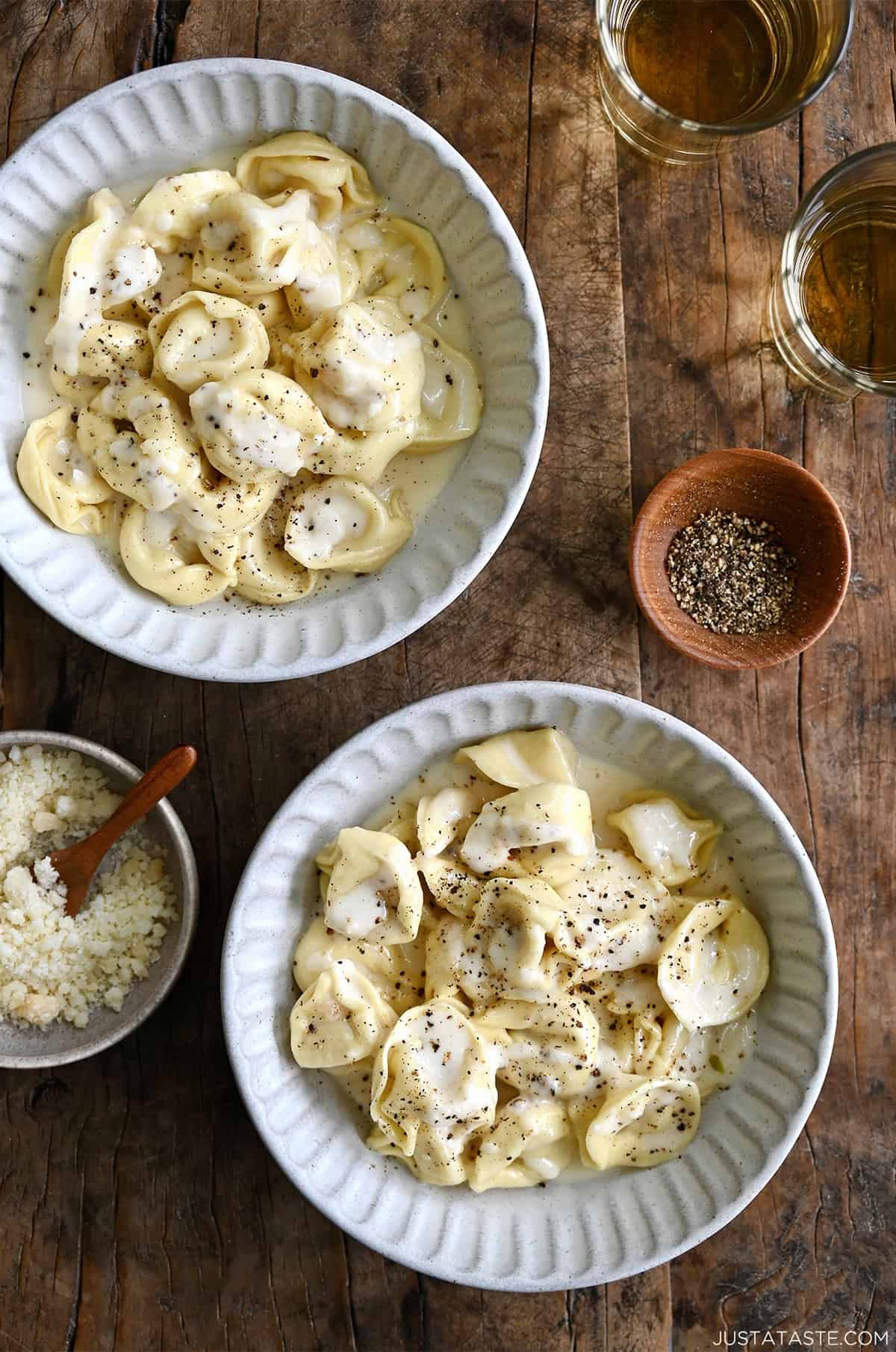 Two bowls containing chicken tortellini alfredo, topped with grated Parmesan and cracked black pepper.
