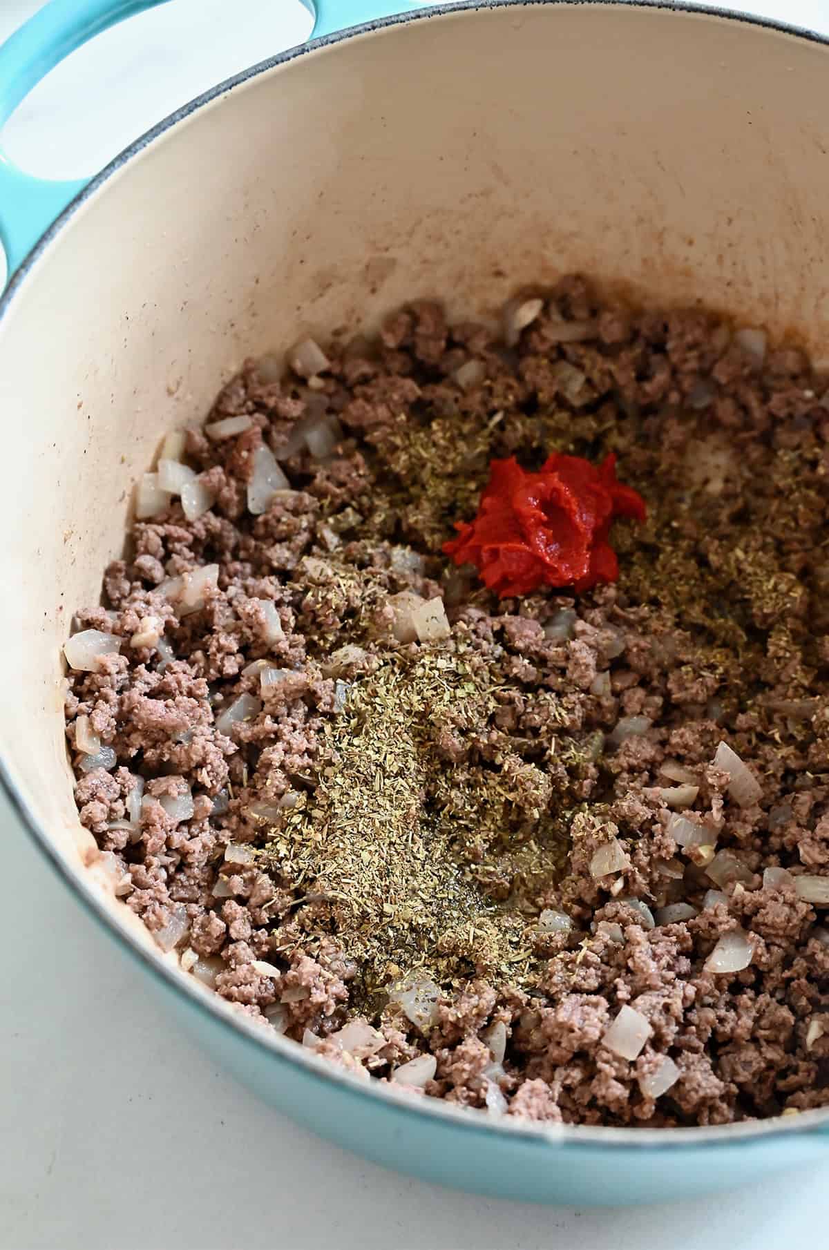 Cooked ground beef in a Dutch oven with tomato paste, Italian seasonings, and sautéed onions and garlic.