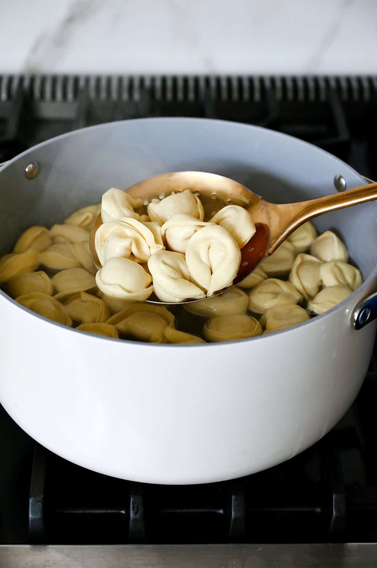 A slotted spoon lifting freshly cooked chicken tortellini from a pot of boiling water.