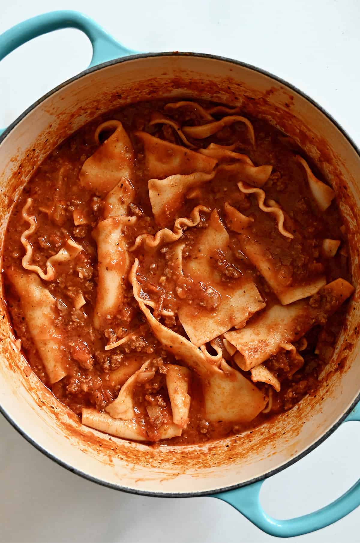 Cooked lasagna noodles in a ground beef tomato sauce in a Dutch oven.