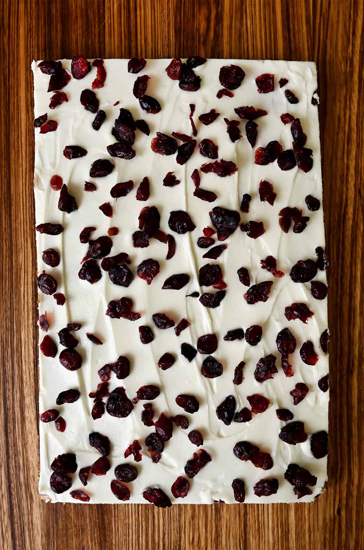 Cranberry bliss bars topped with cream cheese frosting and dried cranberries before being sliced.
