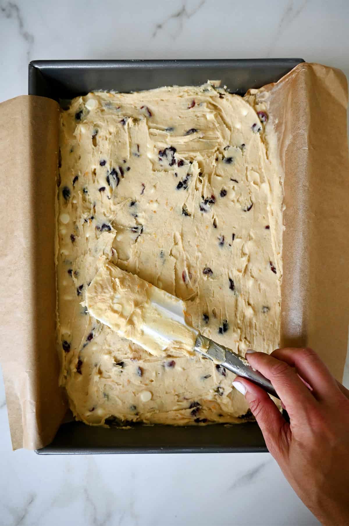 Spreading cranberry bliss blondie batter into a parchment paper-lined 9x13 baking pan.