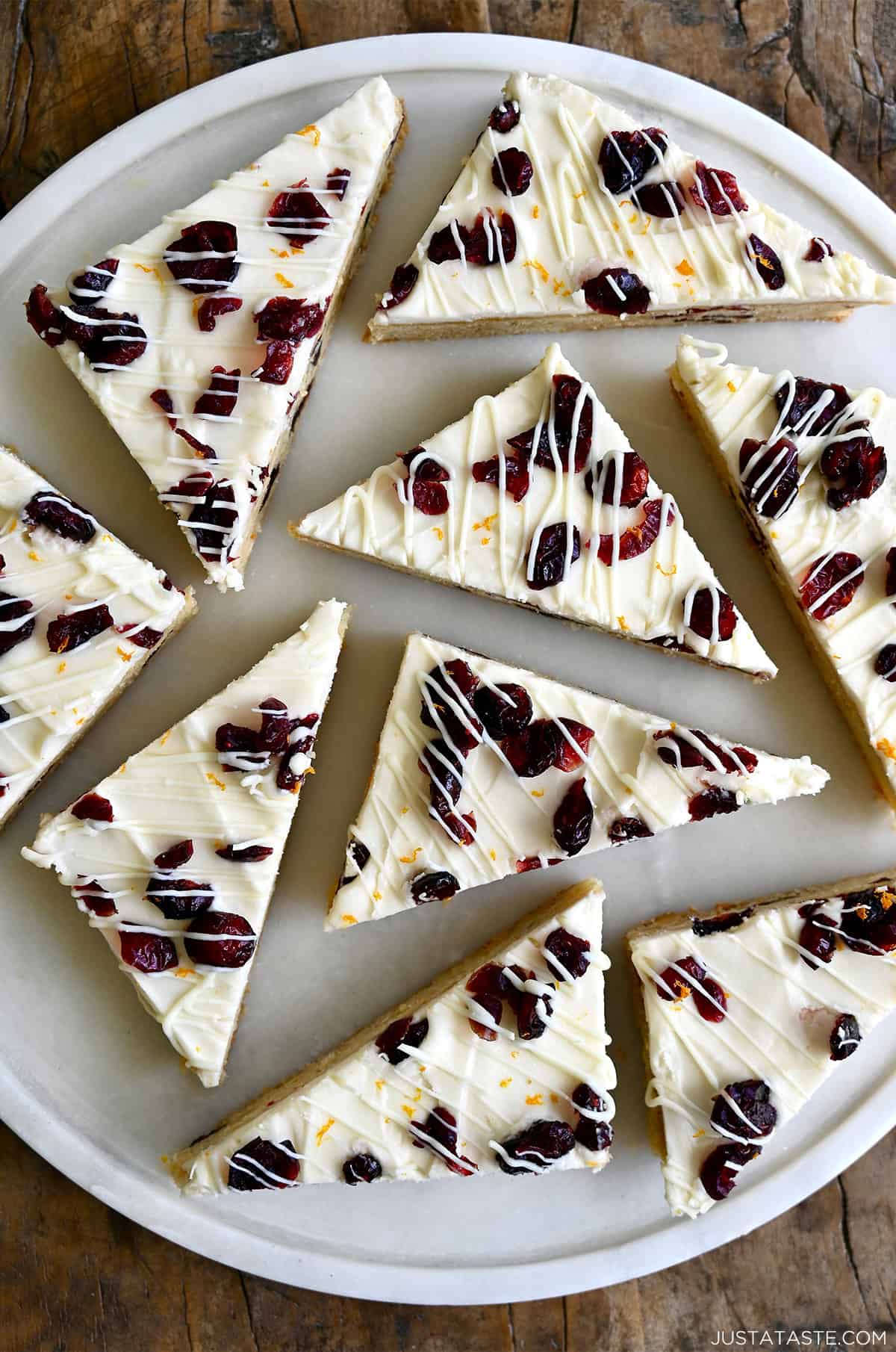 Cranberry Bliss Bars, topped with cream cheese frosting, dried cranberries, a drizzle of white chocolate, and orange zest, cut into triangles.