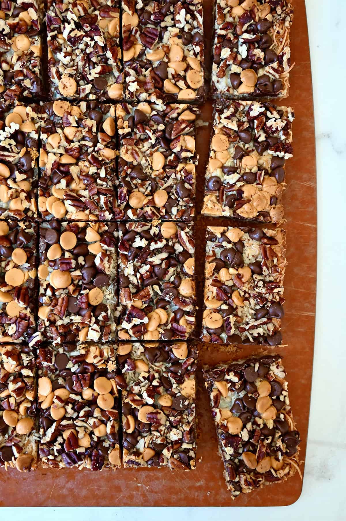 Magic cookie bars cut into squares on a wooden cutting board.