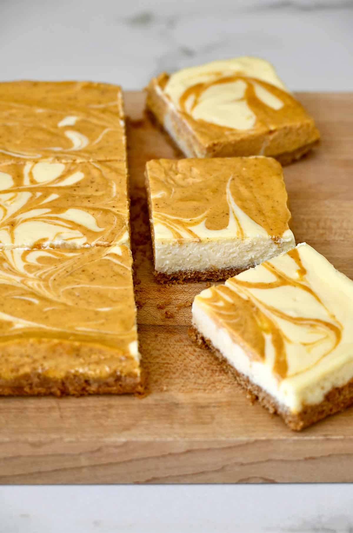 Swirled pumpkin and vanilla cheesecake bars being cut into squares with a sharp knife on a cutting board.
