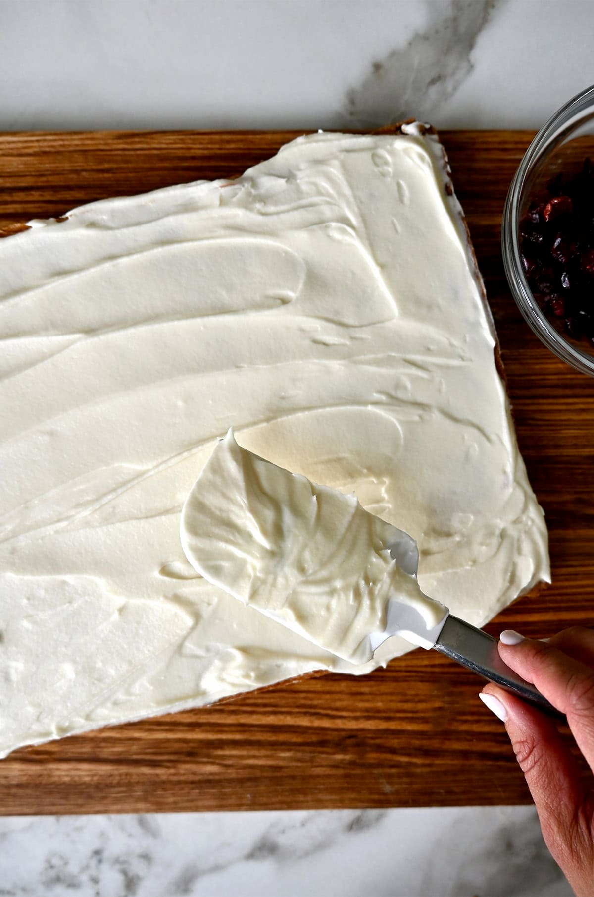 Spreading cream cheese frosting with a spatula onto cranberry bars.