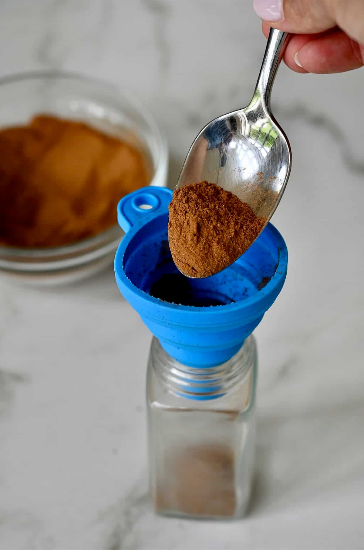 Spooning pumpkin spice into a glass jar using a small funnel.