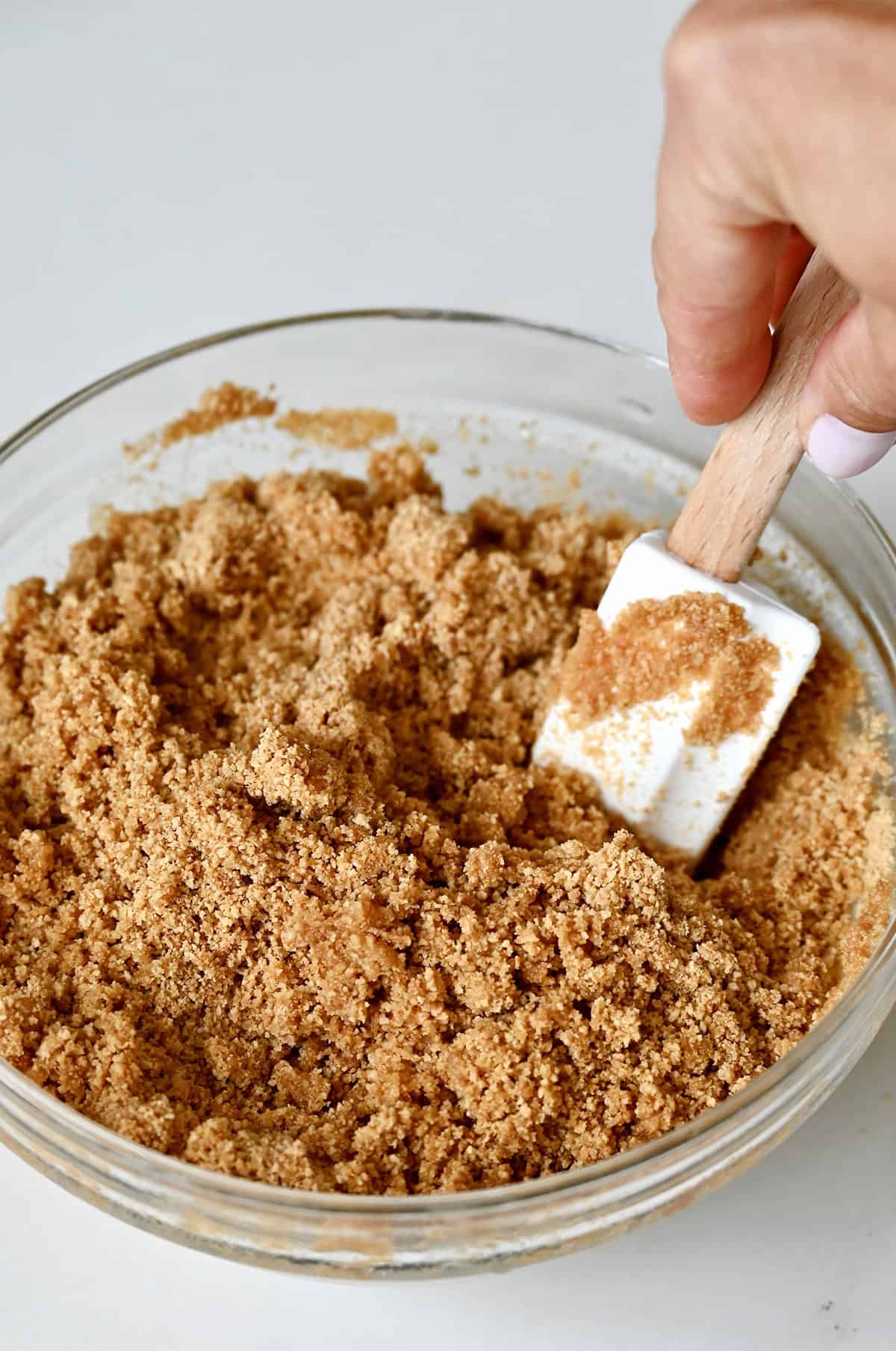 Graham crackers and melted butter being mixed together with a spatula in a glass bowl.