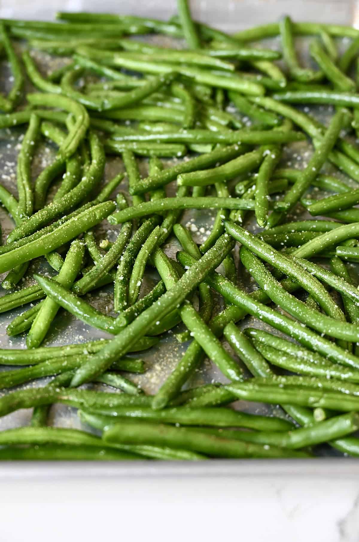 Fresh green beans tossed in olive oil, garlic powder and salt on a baking sheet.
