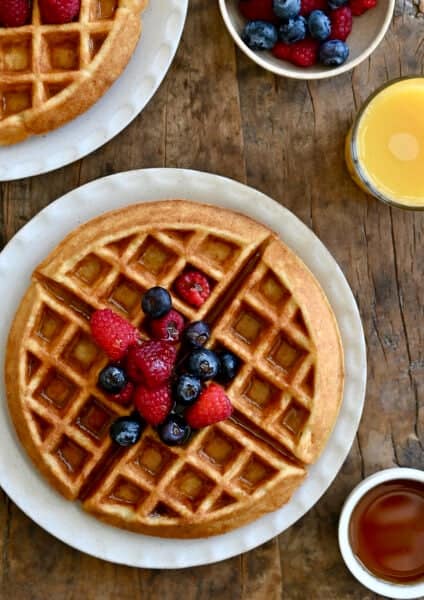 A perfeclty crisp, golden brown protein waffle topped with maple syrup and fresh berries on a large plate.