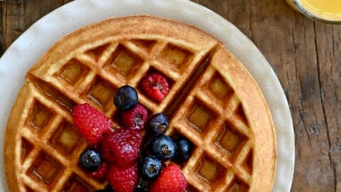 A perfeclty crisp, golden brown protein waffle topped with maple syrup and fresh berries on a large plate.