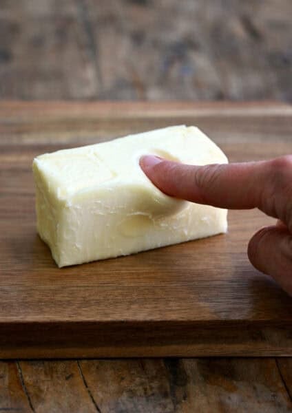 A finger pressing into softened butter to show when it's at the perfect temperature.