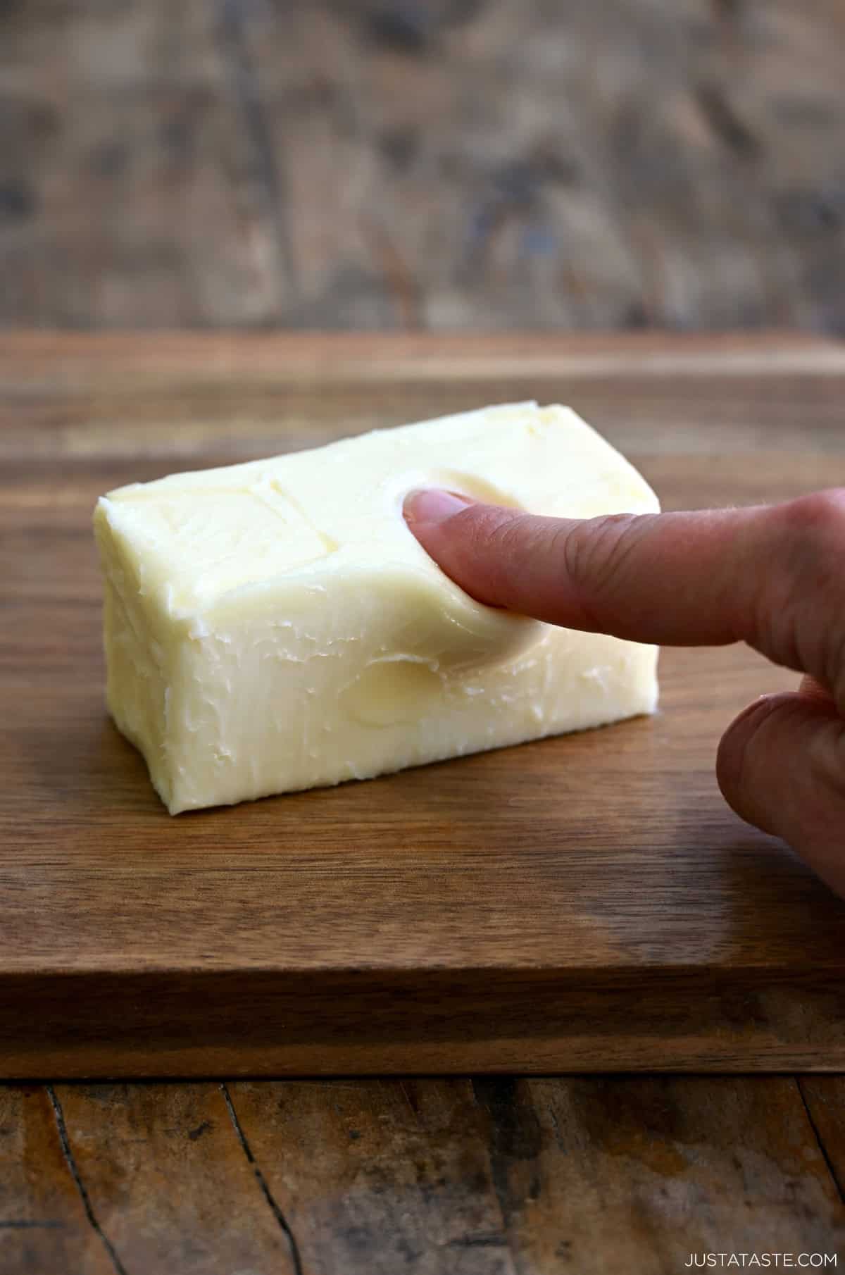 A finger pressing into softened butter to show when it's at the perfect temperature.