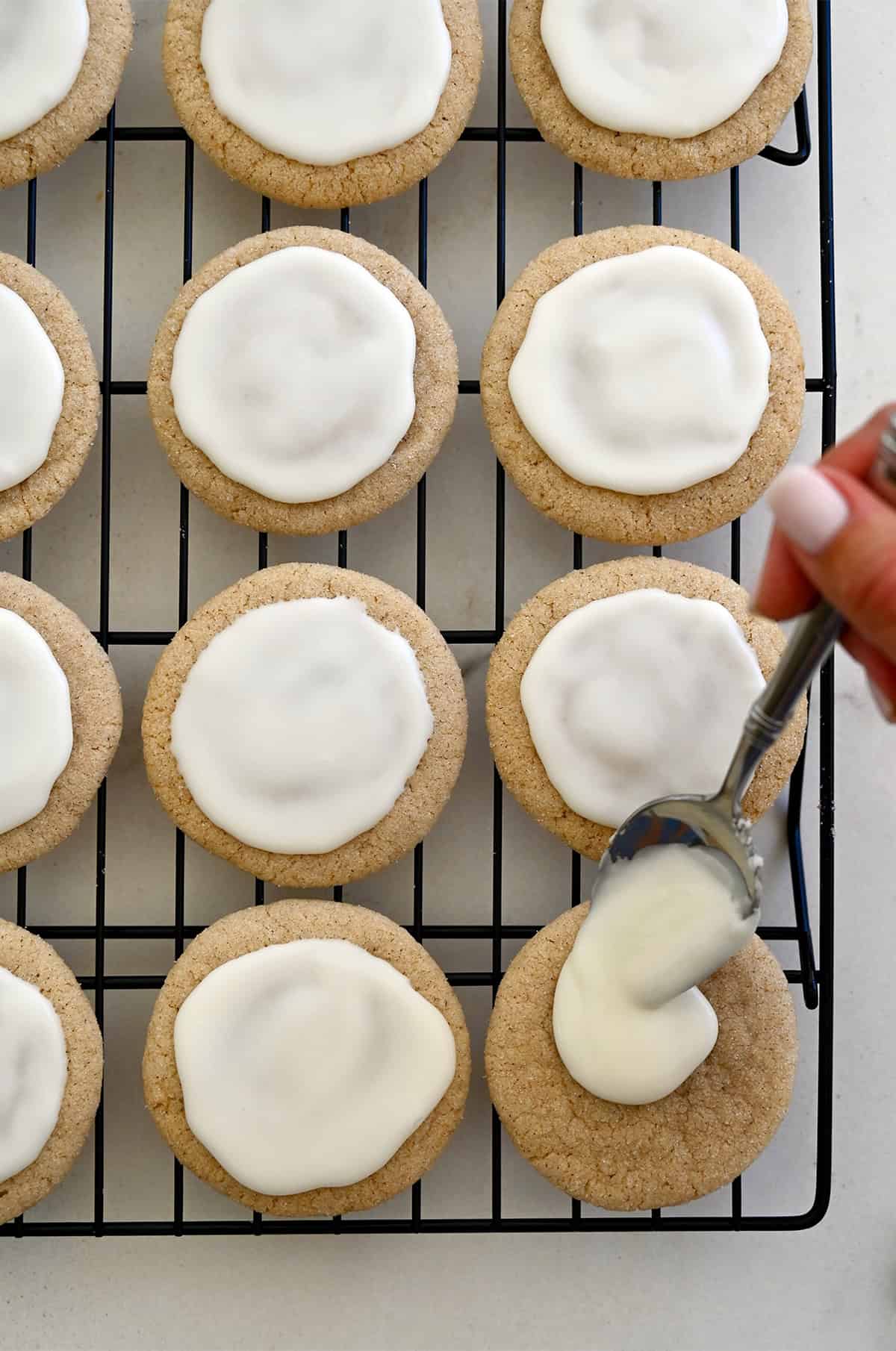 Spooning eggnog glaze over chai sugar cookies on a wire cooling rack.