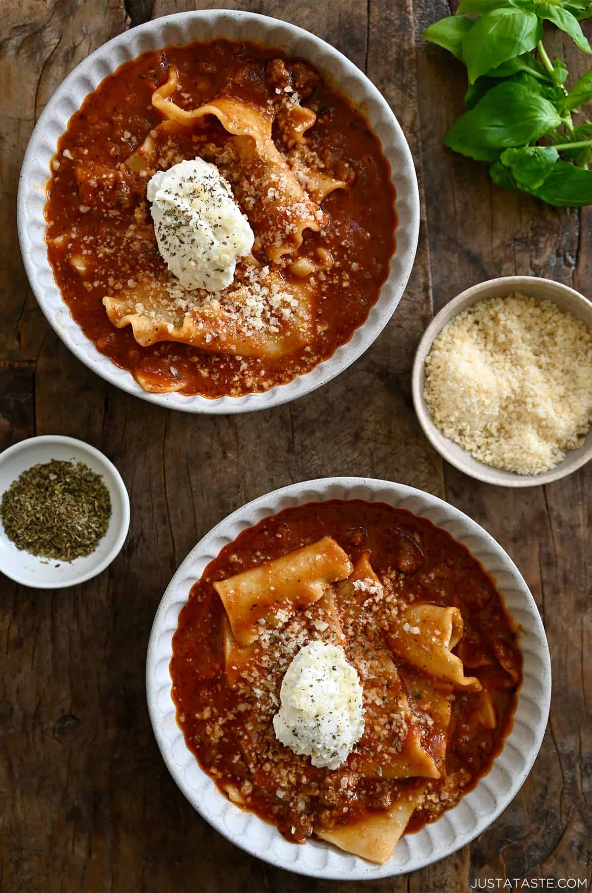 Two bowls containing homemade lasagna soup topped with a dollop of ricotta cheese and grated Parmesan cheese.