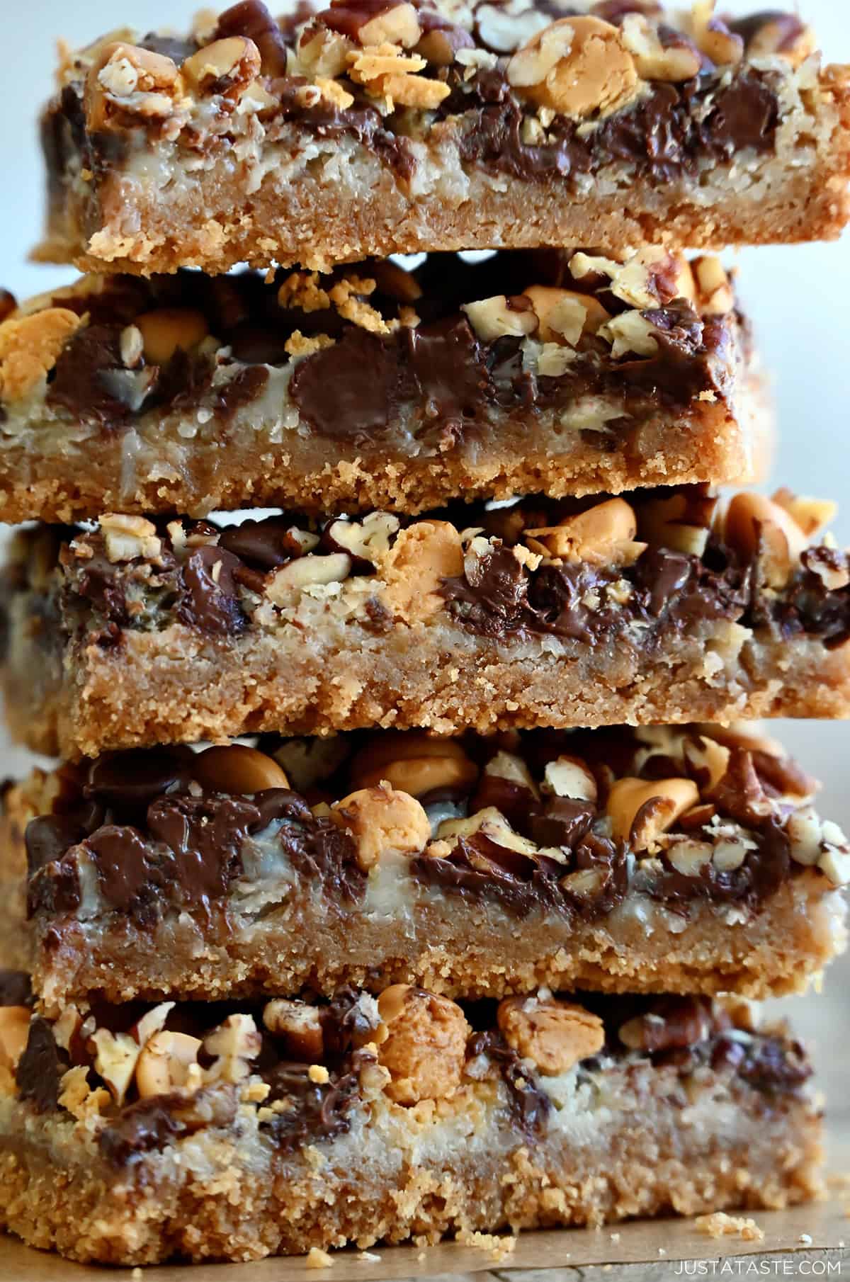 A tall stack of magic cookie bars made with a graham cracker crust, flaked coconut, butterscotch chips, chocolate chips and chopped pecans.