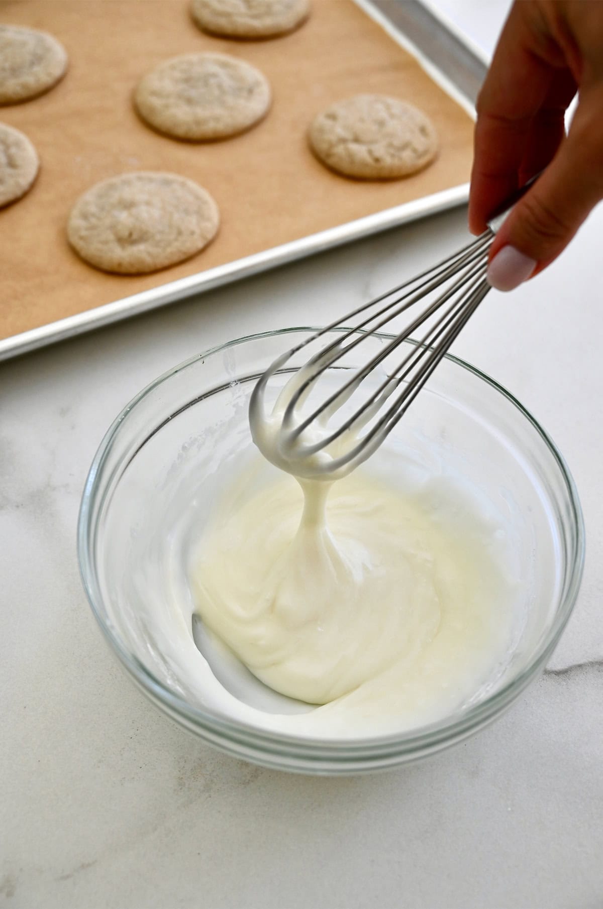 Eggnog icing in a glass bowl near chai cookies cooling on a baking sheet.