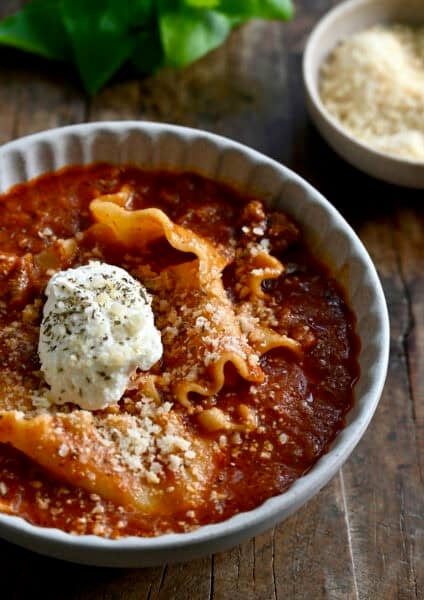 Lasagna soup topped with grated Parmesan and a dollop of creamy ricotta in a bowl.