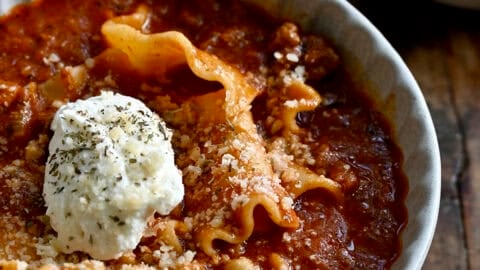 Lasagna soup topped with grated Parmesan and a dollop of creamy ricotta in a bowl.