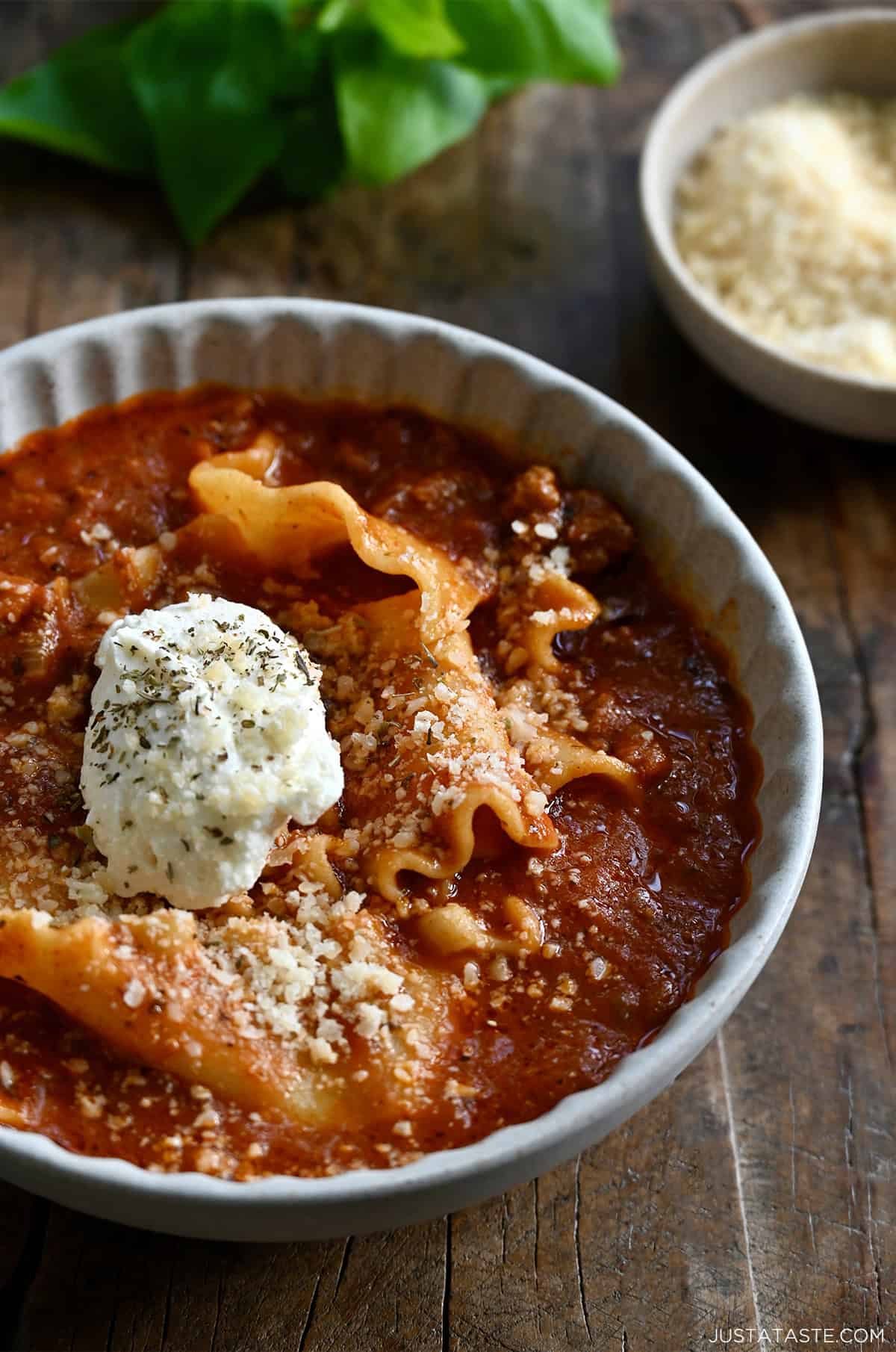Lasagna soup topped with grated Parmesan and a dollop of creamy ricotta in a bowl.