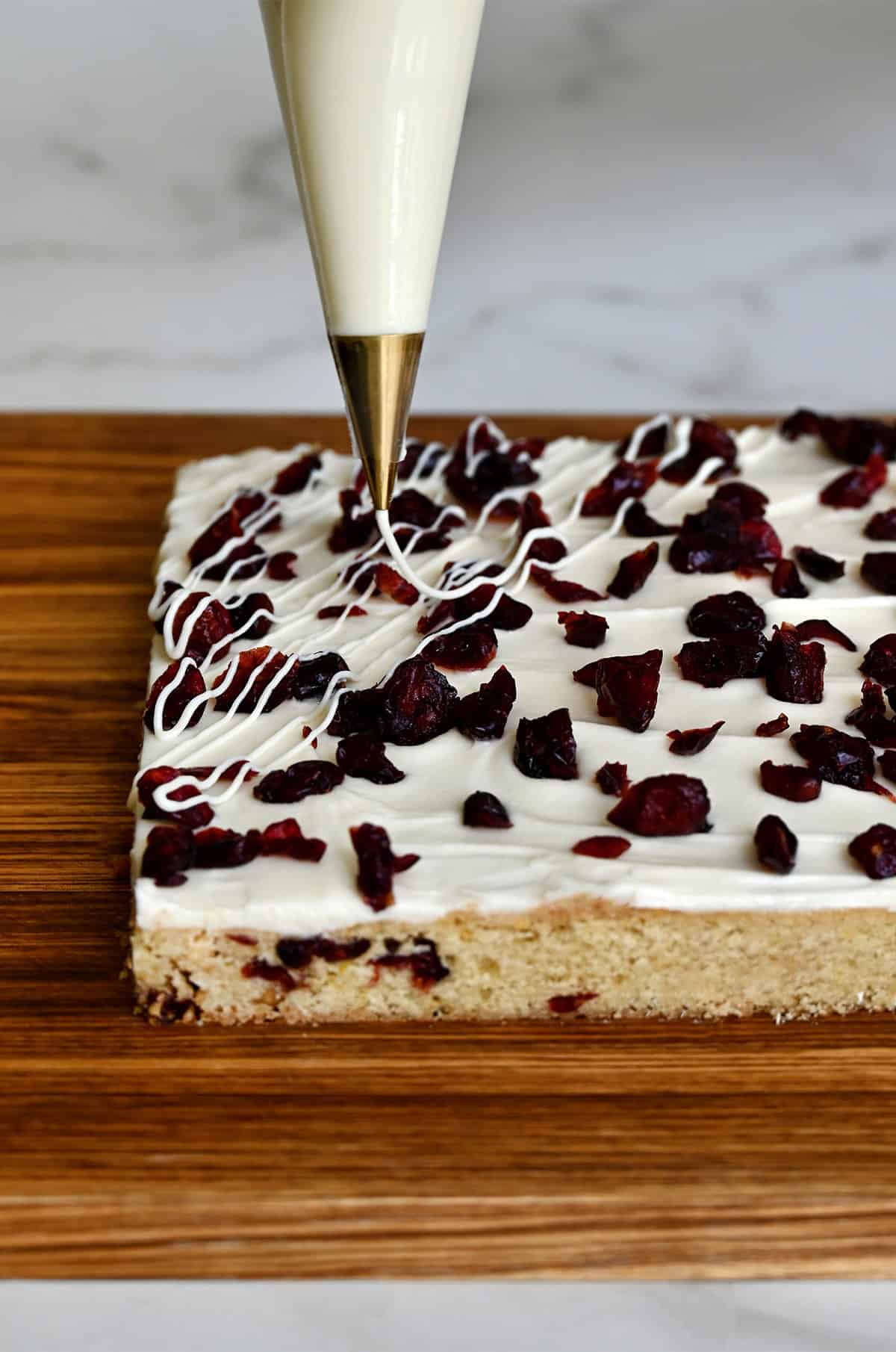 Piping melted white chocolate in a zigzag over cranberry bliss bars.