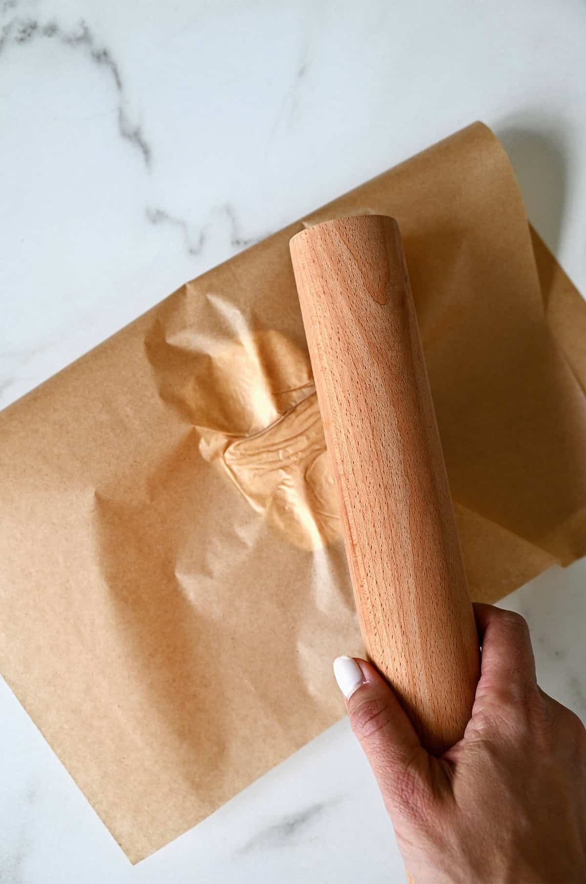 Pounding butter between two sheets of parchment paper with a heavy rolling pin.