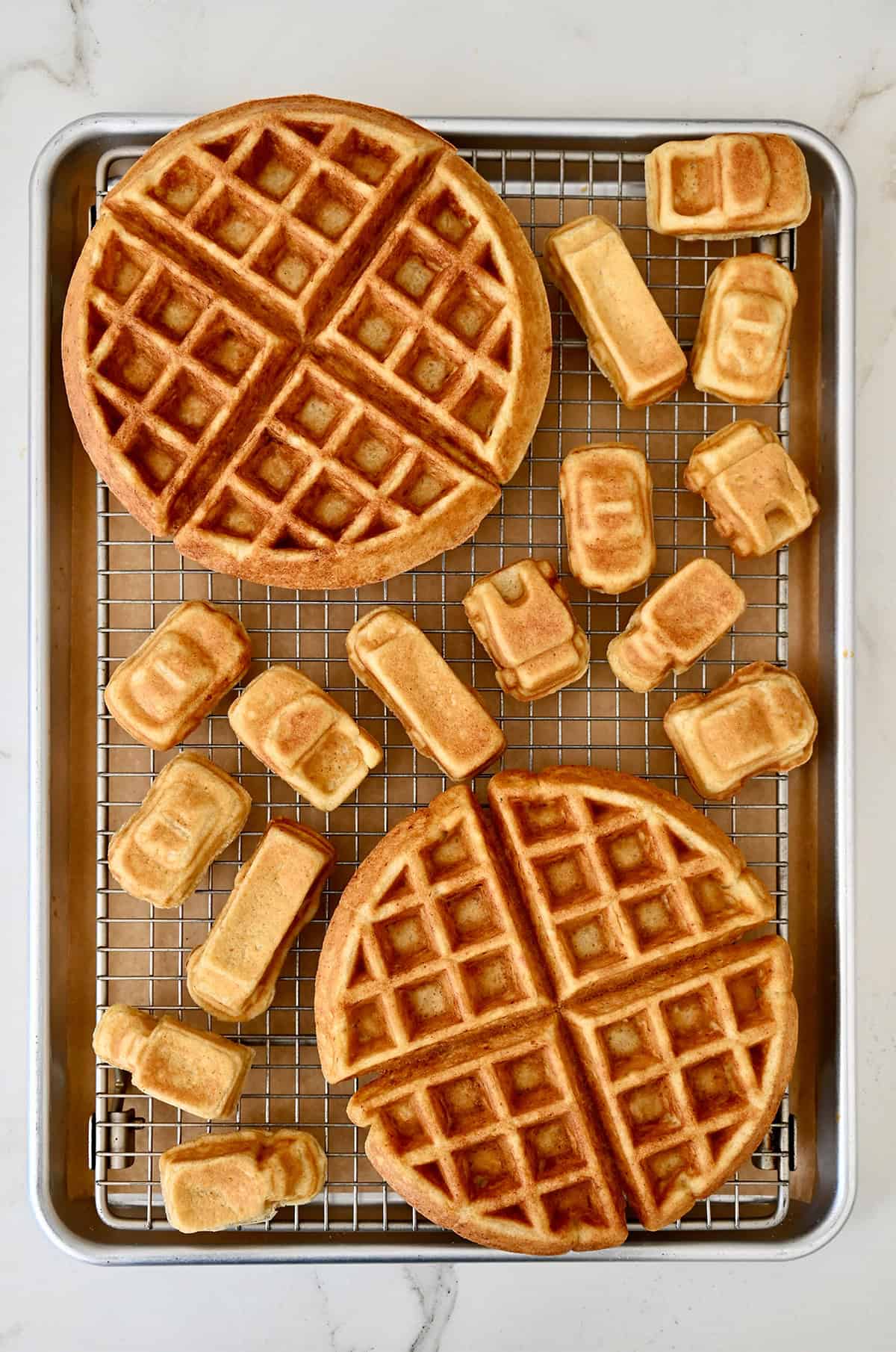 Two Belgian-style protein waffles cooling on a wire rack along with car-shaped waffles.