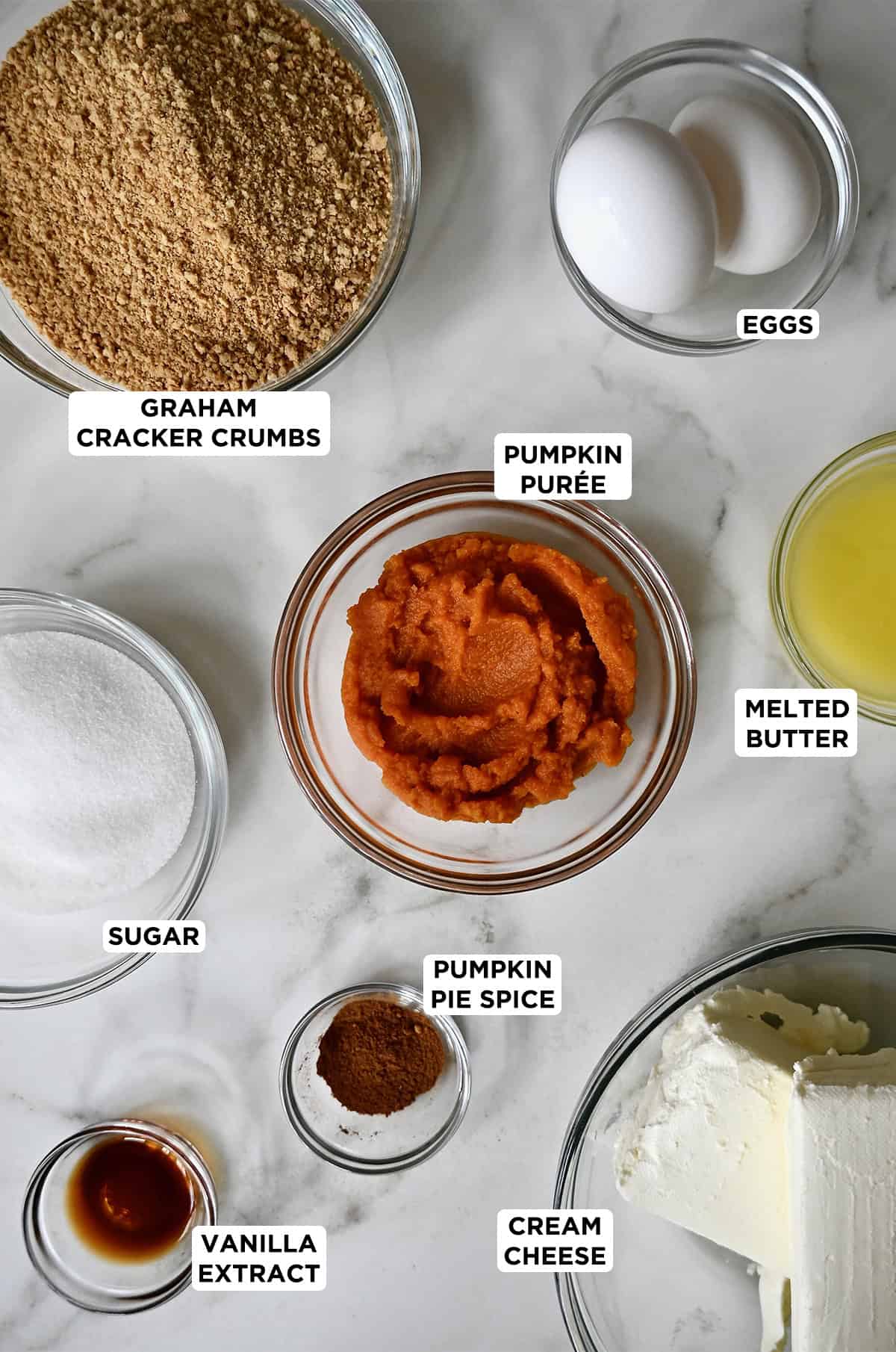 Various sizes of glass bowls containing ingredients to make pumpkin cheesecake bars.