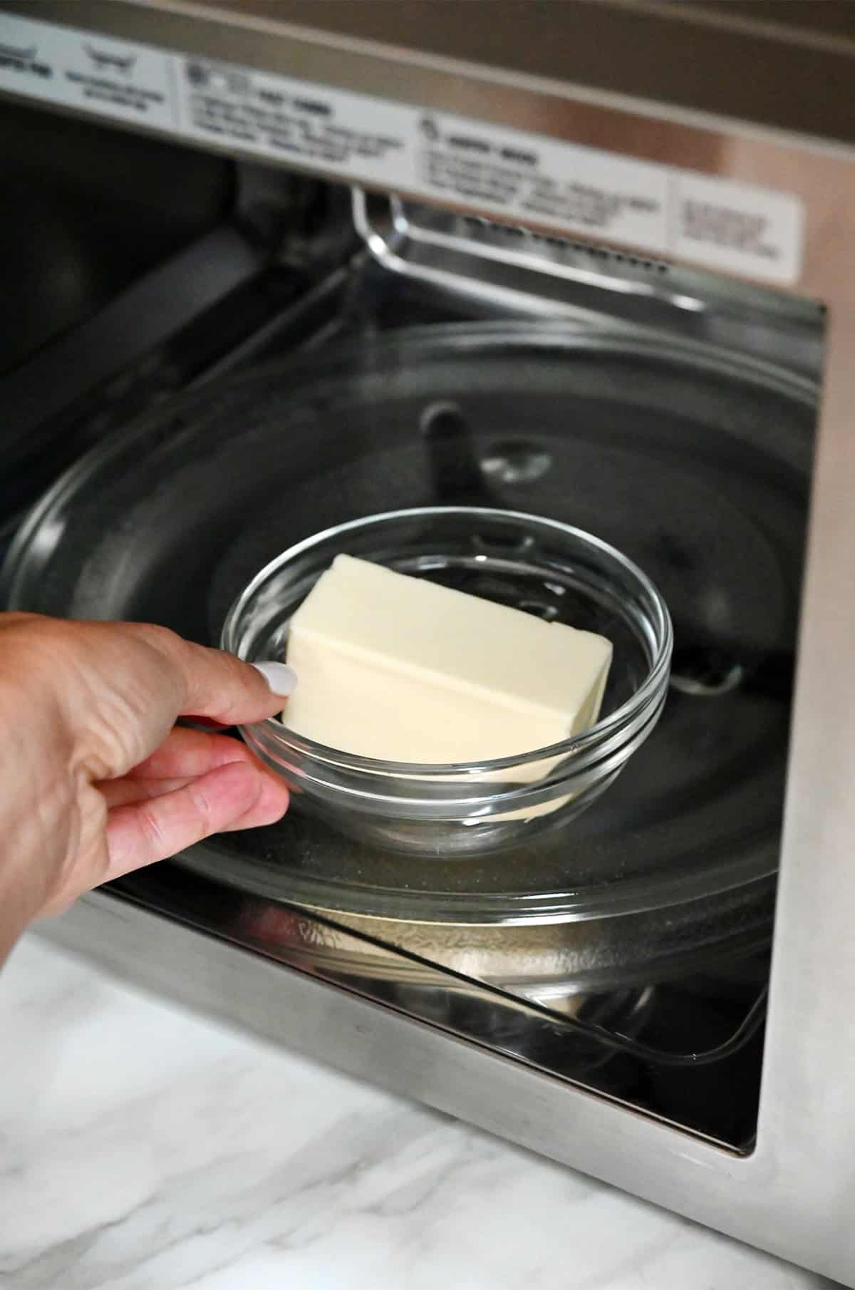 A glass bowl containing a stick of butter is being placed into a microwave.