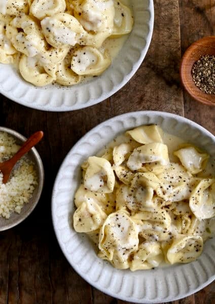 Homemade chicken tortellini Alfredo topped with freshly cracked black pepper and grated Parmesan cheese in a white dinner bowl.