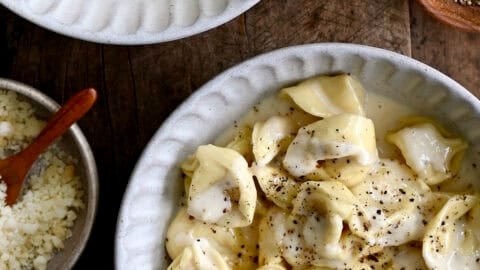 Homemade chicken tortellini Alfredo topped with freshly cracked black pepper and grated Parmesan cheese in a white dinner bowl.