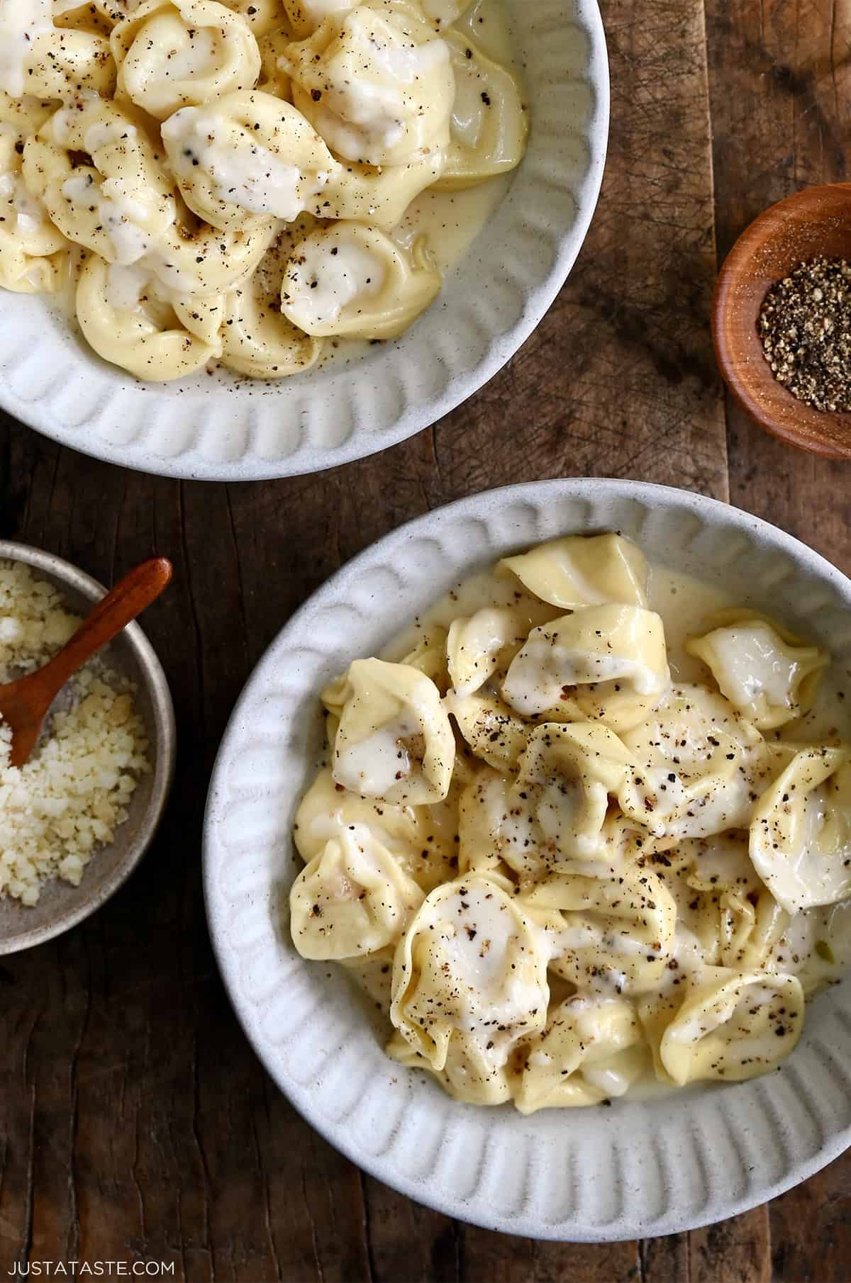 Homemade chicken tortellini Alfredo topped with freshly cracked black pepper and grated Parmesan cheese in a white dinner bowl.